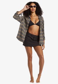 Sorte ternede skjorte, sort bikini-top og sort mini-nederdel. Solbriller og lagdelte halskæder fuldender looket. Hudtonen er tan.