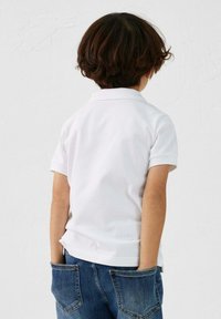 Polo shirt bianco a maniche corte con colletto, abbinato a jeans denim blu. Design semplice, senza motivi visibili e vestibilità standard.