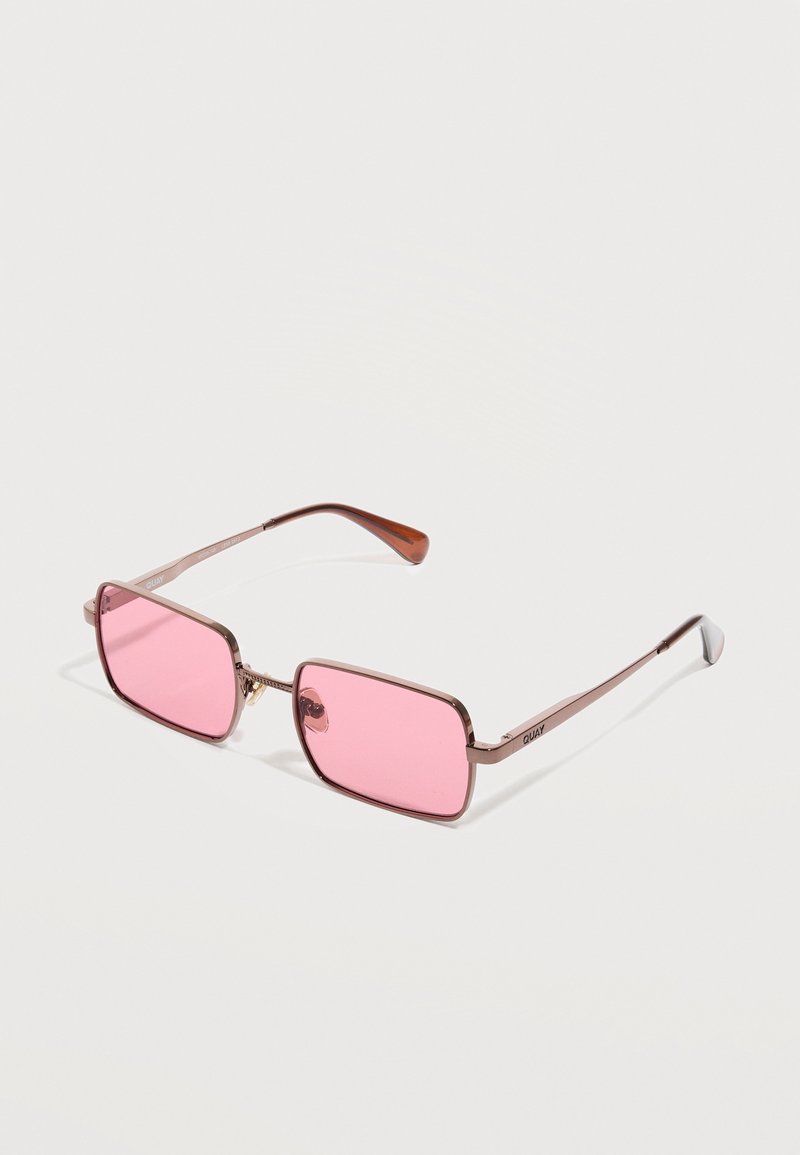 Ορθογώνια γυαλιά ηλίου με μεταλλικό πλαίσιο, ροζ φακούς και λεπτούς βραχίονες, ακουμπούσαν σε λευκό φόντο.