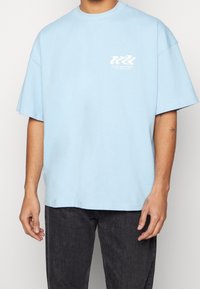 Ljusblå oversized t-shirt med korta ärmar, rund halsringning och vit grafisk tryck på bröstet. Mjuk bomullsmaterial, minimal textur.