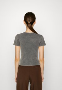 Szara dopasowana koszulka z krótkimi rękawami, okrągłym dekoltem i miękkim, lekko teksturowanym materiałem. Widoczne przeszycia i gładki design z tyłu.