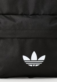 Zwarte stoffen rugzak met een wit Adidas-logo met drie strepen, eenvoudig ontwerp en gestructureerd oppervlak.