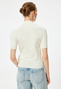 Witte gebreide trui met korte mouwen en een hoge halslijn, gecombineerd met lichtblauwe denim jeans. Gladde textuur en aansluitend ontwerp.