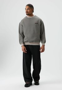 Gestreepte trui in lichtgrijs en zwart, met geribde manchetten en zoom. Gecombineerd met zwarte jeans met wijde pijpen en stevige zwarte schoenen.