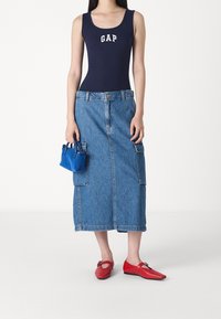 Body senza maniche navy con logo "GAP", gonna maxi in denim blu con tasche laterali e scarpe basse rosse con dettaglio a cinturino. Piccola borsa blu.