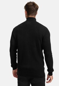 Musta neulottu neulepaita, jossa on korkea kaulus, teksturoitu kuvio sekä resorit hihansuissa ja helmassa. Valmistettu pehmeästä kankaasta, suunniteltu lämmittämään.