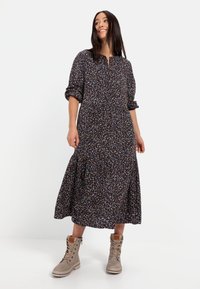 Langärmliges, dunkelblumiges Kleid mit Kragen, gerafftem, gestuftem Rock und leicht puffigen Ärmeln, kombiniert mit hellen Schnürstiefeln.