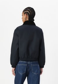 Black bomber jacket with a soft collar, ribbed cuffs, and waistband; paired with high-waisted blue denim jeans.