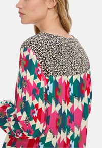 Bunte Bluse mit einem oberen Leopardenmuster und geometrischen Mustern in Pink, Grün und Creme an den Ärmeln und am Körper. Aus weichem Stoff.