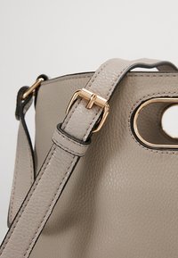 Harmaa nahkainen käsilaukku, jossa on teksturoidun pinnan, kultaiset yksityiskohdat, säädettävä olkahihna ja leikattu yläkahvadesign.