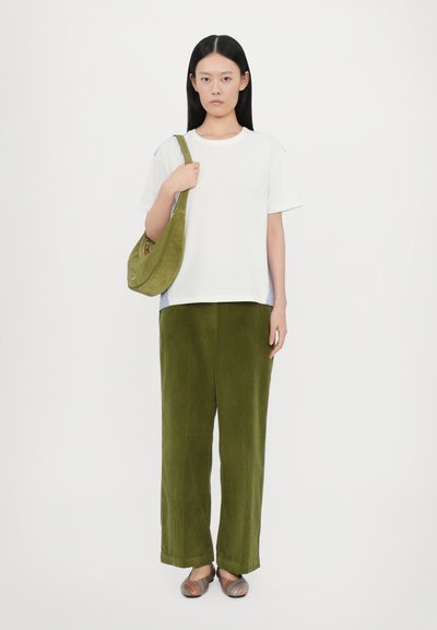 Witte katoenen t-shirt, ruime pasvorm; olijfgroene corduroy broek met brede pijpen; olijfgroene suède hobo tas; meerkleurige gestreepte instappers.