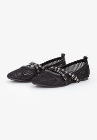 Bailarinas de malla negra con punta afilada, decoradas con tiras entrecruzadas y ojales de metal. Diseño de perfil bajo con una suela lisa.
