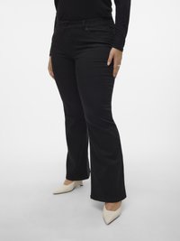 Zwarte uitlopende spijkerbroek met een gladde textuur, voorzien van een ritsvlieger, voorzakken en een lichte stretch. Gecombineerd met off-white puntige hakken.