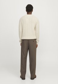 Cream ribbed knit sweater with long sleeves, paired with brown trousers featuring back pockets. The background is plain white.
