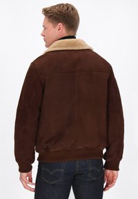 Jachetă bomber din suede maro, cu guler din blană bej, manșete și tiv cu nervuri, având un design curat și croi ajustat pe spate.