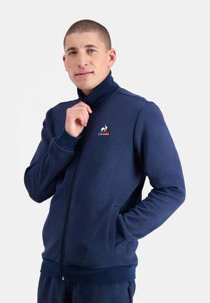 Navy blue zip-up sweatshirt in smooth fabric, featuring a high collar, side pockets, and a logo on the left chest.