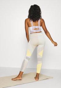 Sportovní legíny a crop top v světle šedé barvě se žlutými a šedými geometrickými vzory. Top má logo postavy a výřez na zádech.