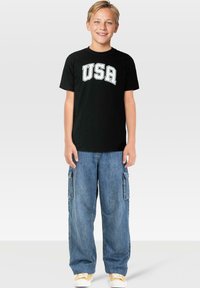 Svart bomull t-shirt med "USA" i vit bågformad text, parat med löst sittande denim cargobyxor med sidofickor.