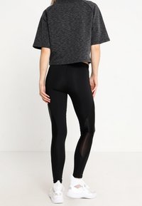 Czarny crop top z krótkimi rękawami, zestawiony z dopasowanymi czarnymi legginsami z siateczkowymi wstawkami i teksturowanymi akcentami. Białe sneakersy.