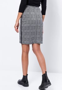 Jupe écossaise mi-longue en noir et blanc avec une fente sur le côté et un tissu texturé. Associée à des bottines noires.