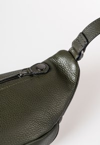 Borsa in pelle verde scuro con finitura testurizzata, dotata di chiusura a zip e di una tracolla piatta con fastener in metallo. Finitura arrotondata.
