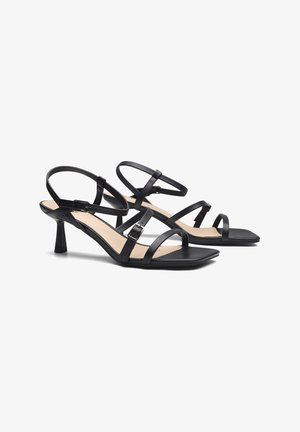 Sandales à talons noires avec plusieurs brides, une fermeture à boucle et une semelle intérieure texturée. Les talons sont d'une hauteur modeste avec une forme carrée.