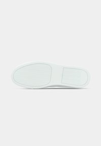 Semelle de basket blanche présentant un motif de grip texturé, une forme ovale et une finition lisse ; comprend des zones de hachures surélevées pour la traction.