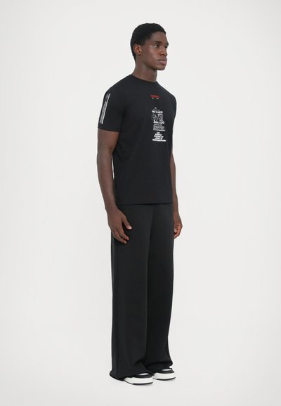 Black cotton t-shirt with printed text graphic on the front and sleeve, paired with black wide-leg pants and black and white sneakers.