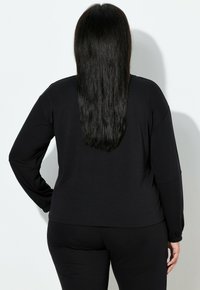 Top nero a maniche lunghe realizzato in tessuto morbido, con vestibilità comoda e design con spalle scese. Abbinato a pantaloni neri coordinati.