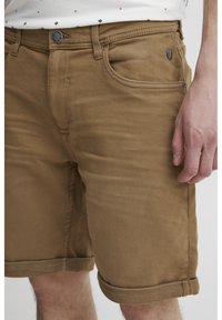 Braune Baumwollshorts mit glatter Textur, umschlagbaren Bündchen, Fronttaschen und einem Knopfverschluss mit metalischem Akzent.