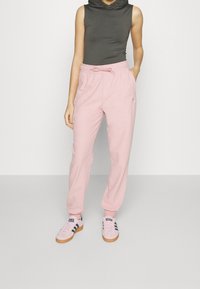 Light pink joggers with an elastic waistband and drawstring, made of soft fabric; paired with gray sleeveless top and pink shoes.