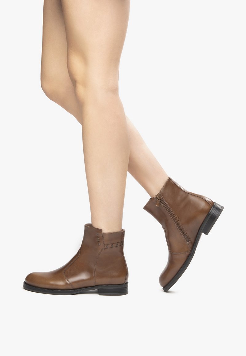 Stivaletti in pelle marrone alla caviglia con zip laterale, punta tonda, cuciture decorative e sottili dettagli con borchie. Suola in gomma bassa e piatta.