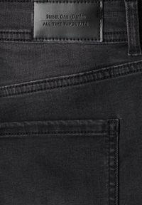 Gros plan sur la poche arrière d'un jean en denim noir avec une étiquette en cuir noir cousue indiquant Street One Denim All Time Favourite.