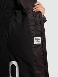 Svart vadderad jacka med ribbad struktur, utrustad med en zip-ficka, inre etikett med text och djärv vit siffra på fodret.