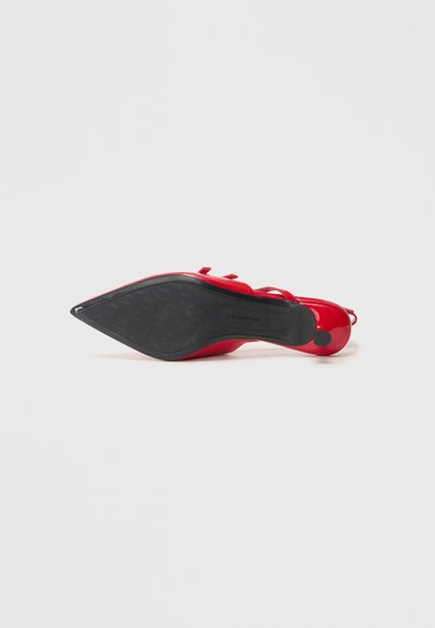 Red high-heeled shoe with a pointed toe, glossy upper, and textured black sole. Features thin straps and a round heel accent.