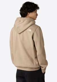 Felpa con cappuccio in tessuto beige, con una finitura leggermente strutturata e polsini a costine. Logo del marchio stampato sulla parte superiore della schiena.