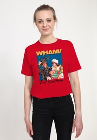 Kobieta ubrana w czerwoną koszulkę z członkami zespołu Wham! w kostiumach świątecznych z prezentami i napisem "Ostatnie Święta".