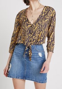 Brown and yellow patterned button-up shirt with a tie-front design, paired with a blue denim A-line skirt featuring distressed details.