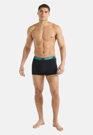 Zwarte boxershorts met een turquoise tailleband met een logo. De stof lijkt glad en de pasvorm is nauwsluitend, ontworpen voor comfort.