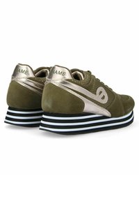 Olijfgroene sneakers met metallic zilveren accenten, textuurpanelen en een gestreepte zwart-witte platformzool. Inclusief merkdetail aan de achterzijde.