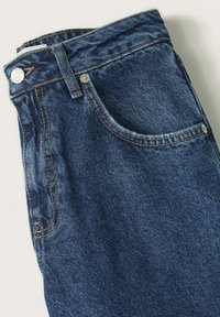 Složené tmavě modré džíny ukazující přední kapsu, poutek na opasek, knoflík a detailní švy na světlém pozadí.