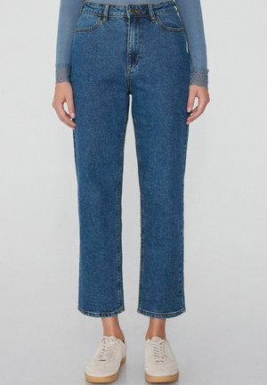 Hoge taille blauwe denimjeans met rechte pijpen, lichte slijtage, klassiek vijf-pocket ontwerp en sluiting met bovenste knoop. Gekombineerd met witte sneakers.