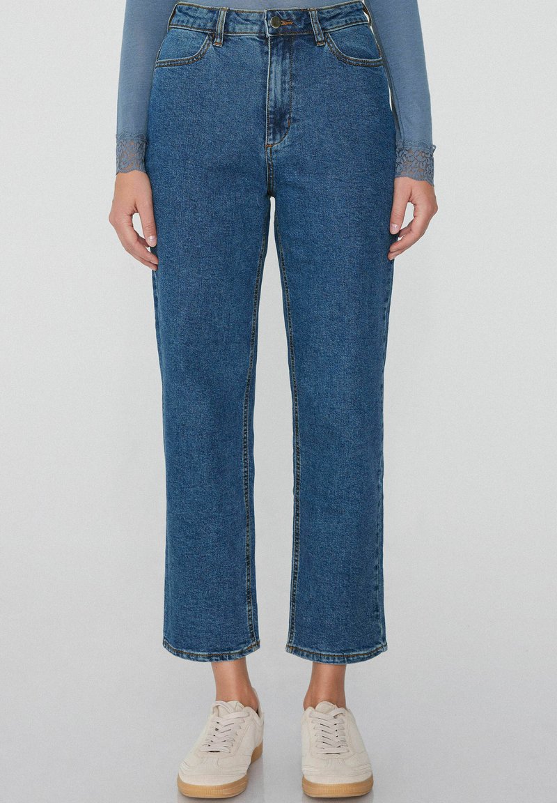 Džíny s vysokým pasem, modré denimové, se rovnými nohavicemi, mírným opotřebením, klasickým designem s pěti kapsami a zapínáním na horní knoflík. V kombinaci s bílými teniskami.