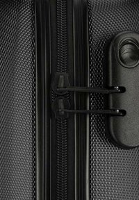 Valigia nera con superficie texturizzata a motivo diamante, zip resistente e accessori in plastica nera.