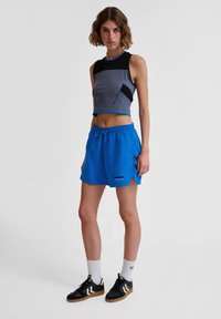 Grå kortärmad topp med svarta accenter och blå kant, ihopparad med blå shorts med en logotyp, sidoöppningar och svarta sneakers.