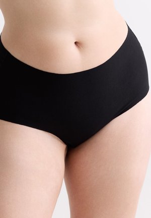 Unterer Torso einer Frau, die schlichte schwarze, hoch taillierte Unterwäsche trägt, zeigt natürlichen Hautton und Nabel vor hellem Hintergrund.