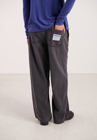 Čierne široké rifľové nohavice s kontrastným šitím a veľkým zadným vreckom s nálepkou. Kombinované s dlhým modrým tričkom.