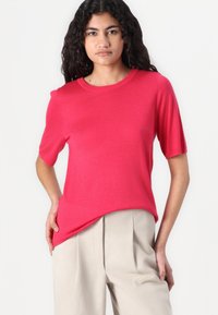 Fuchsia short-sleeve sweater made of lightweight fabric, featuring a rounded neckline and relaxed fit, paired with beige high-waisted trousers.