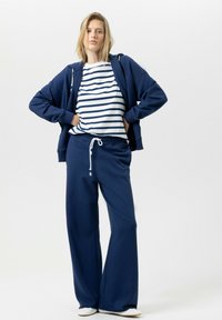 Marineblauwe hoodie, gestreept wit-marineblauw T-shirt en wijd uitlopende marineblauwe joggingbroek met trekkoord. Zachte stof, casual ontwerp, minimale details.