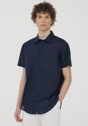 Camicia a maniche corte con bottoni di colore blu navy, realizzata in tessuto testurizzato, con colletto regular e orlo arrotondato, caratterizzata da discreti dettagli con bottoni.